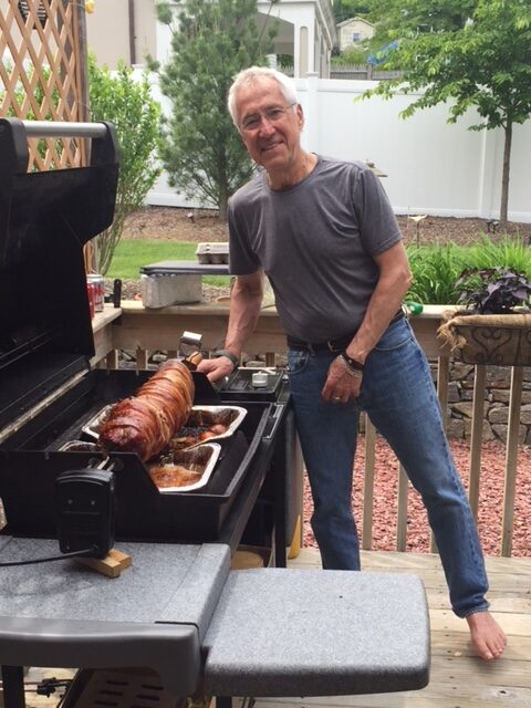 A man standing next to an open grill with food on it.